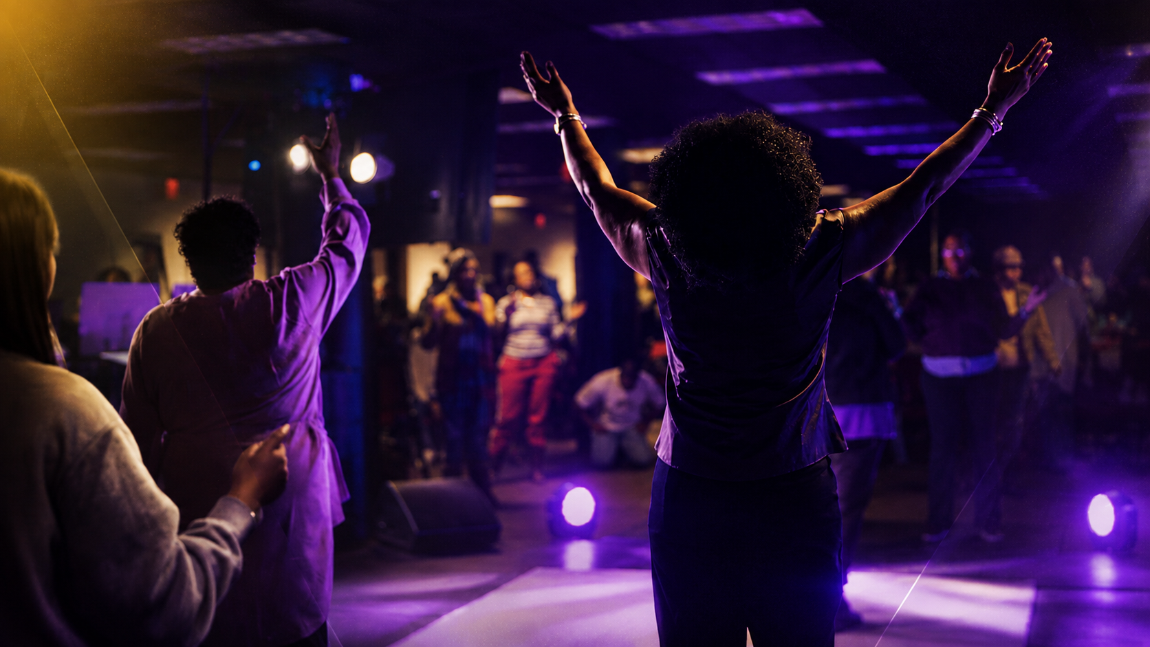 Worshippers with hands raised in purple stage light at New Vision International Ministries
